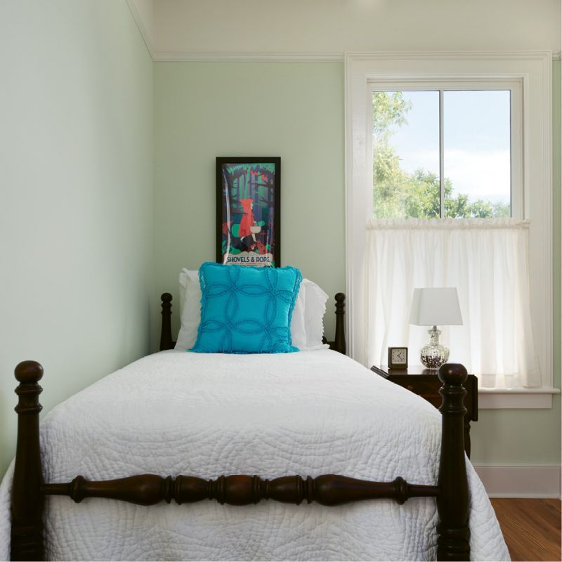 In this petite guest room, a vintage twin bed with a carved pineapple motif and a Shovels & Rope poster add local flavor.