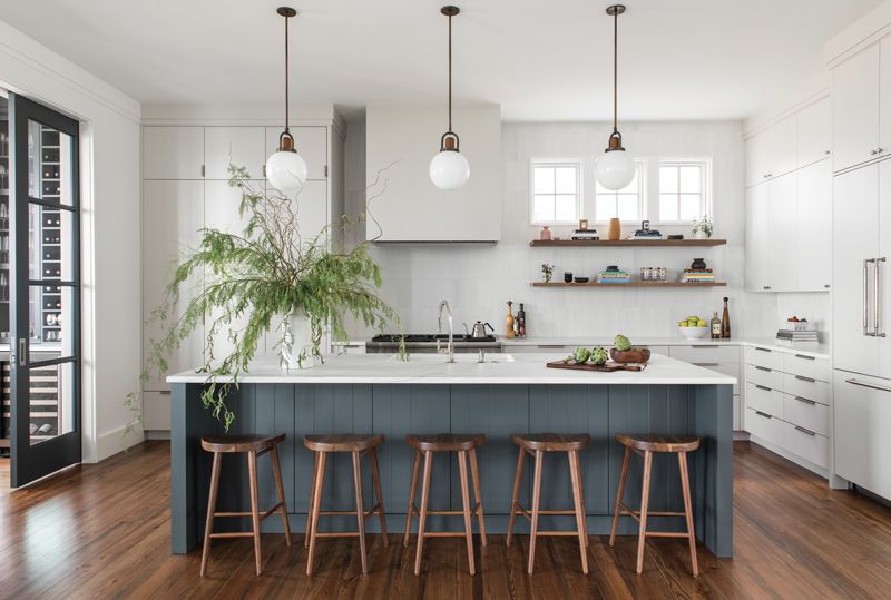 Chill Space: A selection of soft white paints (walls are Benjamin Moore “Chantilly Lace,” cabinets, Farrow & Ball “Ammonite”), combined with warm woods, bronze accents, and a pop of color courtesy of the island, create a sense of coziness in this open-plan kitchen.